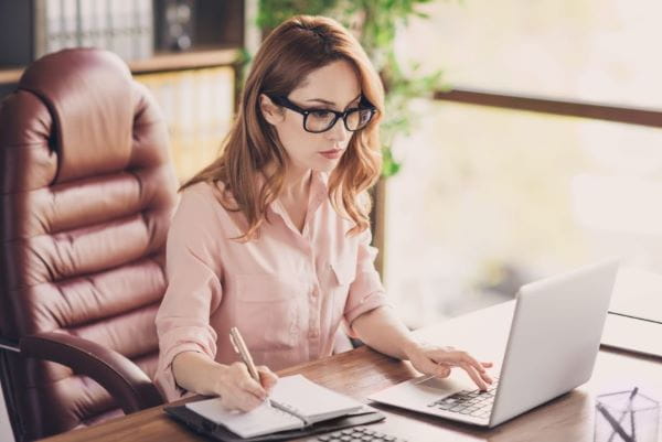 Getty image of woman on laptop and holding pen on notepad