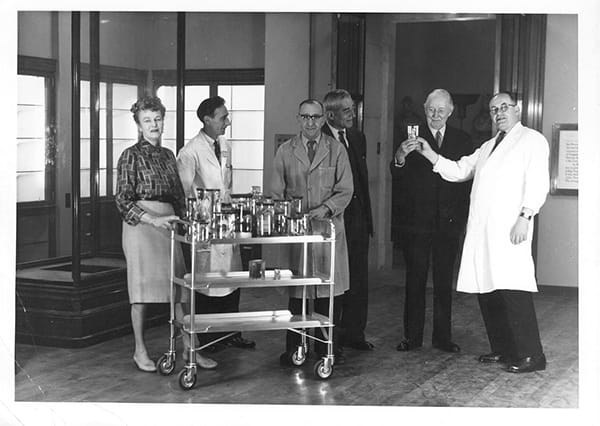 Monochrome photograph of 5 men and 1 women with a trolley of preserved specimens.